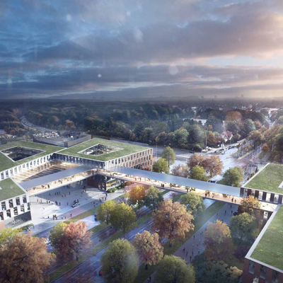Eine Luftaufnahme eines modernen Gebäudekomplexes umgeben von Bäumen und Straßen. Die Architektur zeigt flache, grüne Dächer und eine zentrale Fußgängerbrücke, die verschiedene Bereiche miteinander verbindet. Der Himmel ist bewölkt, was eine stimmungsvolle Atmosphäre erzeugt.