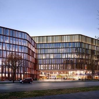 Moderne, mehrstöckige Gebäude mit großen Glasflächen und einer geschwungenen Fassade. Die Architektur kombiniert Holz und Glas, um ein einladendes Ambiente zu schaffen. Im Vordergrund sind Bäume und eine Straße mit Autos zu sehen. Der Himmel ist in sanften Farben des Sonnenuntergangs.