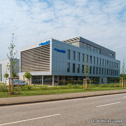 Moderne, mehrstöckige Bürogebäude mit großen Fenstern. Der Schriftzug „condair“ ist deutlich sichtbar. Vor dem Gebäude befinden sich Grünflächen und kleine Bäume. Der Himmel ist teilweise bewölkt.