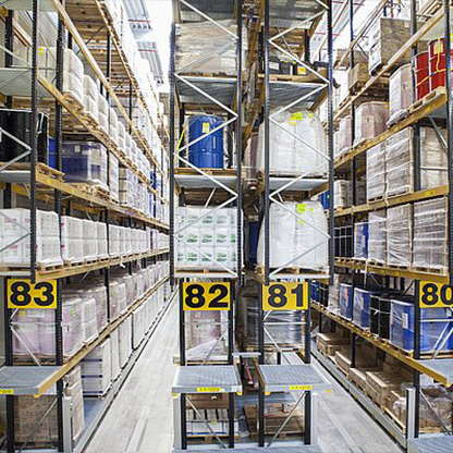 Ein lagerähnlicher Bereich mit hohen Regalen, die mit verschiedenen Produkten in Kisten und Fässern gefüllt sind. Die Regale sind nummeriert (80 bis 83), und der Boden ist aus hellem Holz oder Laminat. Der Raum ist gut beleuchtet und ordentlich.