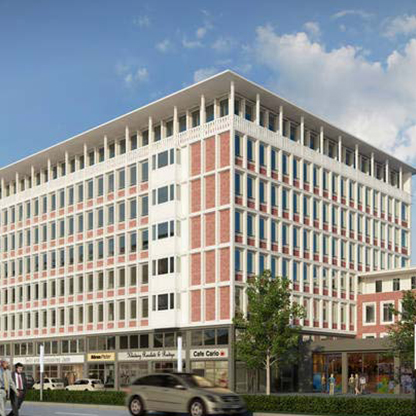 Moderne Gebäude mit mehreren Stockwerken, charakterisiert durch eine Fassade aus roten Ziegeln und großen Fenstern. Im Erdgeschoss sind geschäftliche Einrichtungen und gemütliche Terrassen zu sehen. Der Himmel ist klar mit wenigen Wolken.