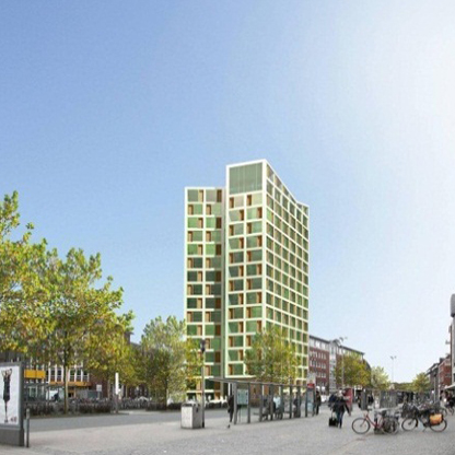 Moderne Wohn- oder Geschäftsbebauung in einem urbanen Umfeld. Der Gebäudeentwurf ist von grünen und goldenen Elementen geprägt. Im Vordergrund sind einige Bäume und Passanten, darunter Fahrräder und Wartehäuschen, sichtbar. Der Himmel ist klar und blau.