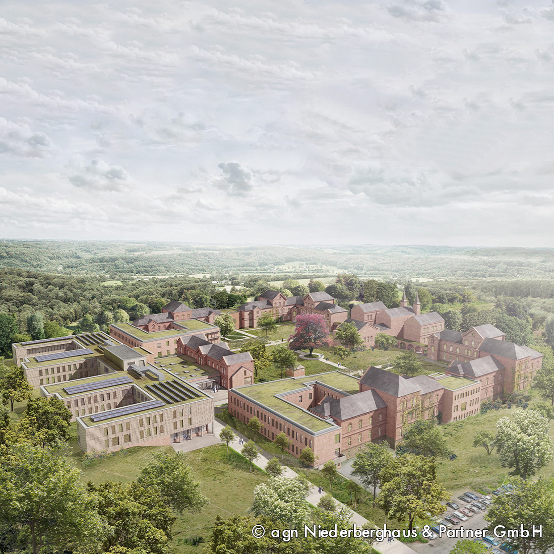 Luftaufnahme eines großen, modernen Gebäudekomplexes, umgeben von Wäldern. Die Architektur kombiniert historische und zeitgenössische Elemente. Im Vordergrund gibt es grüne Rasenflächen und Bäume, während im Hintergrund eine Landschaft mit sanften Hügeln zu sehen ist.