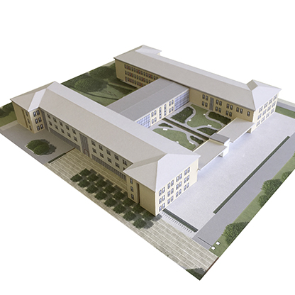 Modell eines Gebäudekomplexes mit mehreren rechteckigen Gebäuden, die um einen zentralen Innenhof angeordnet sind. Der Innenhof ist mit Grünflächen und Wegen gestaltet. Die Gebäude haben eine helle Fassade und sind von einem rechteckigen Bereich aus gepflastertem Boden umgeben.