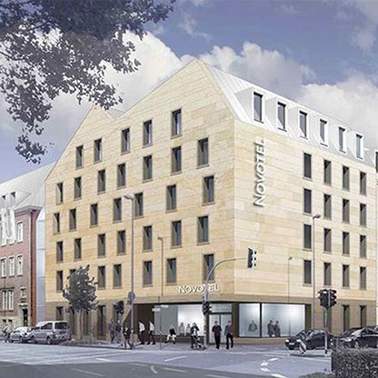 Eine moderne Fassade eines Novotel-Hotels mit hellen Sandsteinplatten. Das Gebäude hat mehrere Fenster und ist vierstöckig. Unterhalb sind Schilder mit dem Schriftzug „Novotel“ zu sehen. Autos parken auf der Straße und Passanten bewegen sich in der Nähe.
