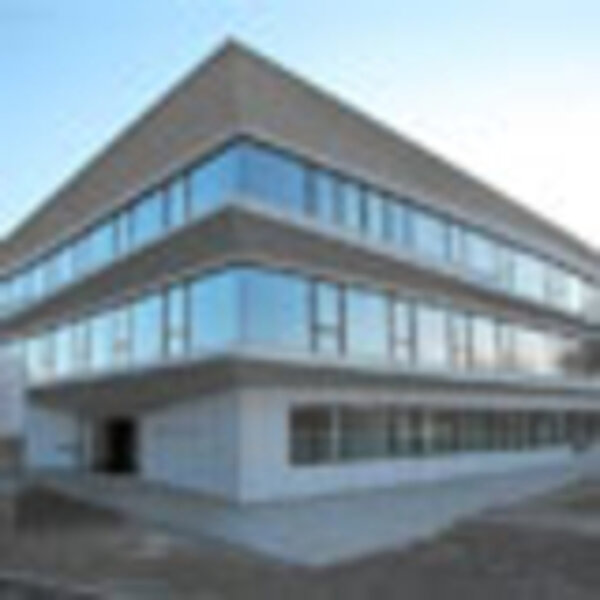 Eine moderne, dreigeschossige здание mit großen Glasfenstern und einem minimalistischen Design. Das Gebäude hat eine helle Fassade und befindet sich in einem klaren Himmelshintergrund. Der Eingang ist auf der linken Seite sichtbar.