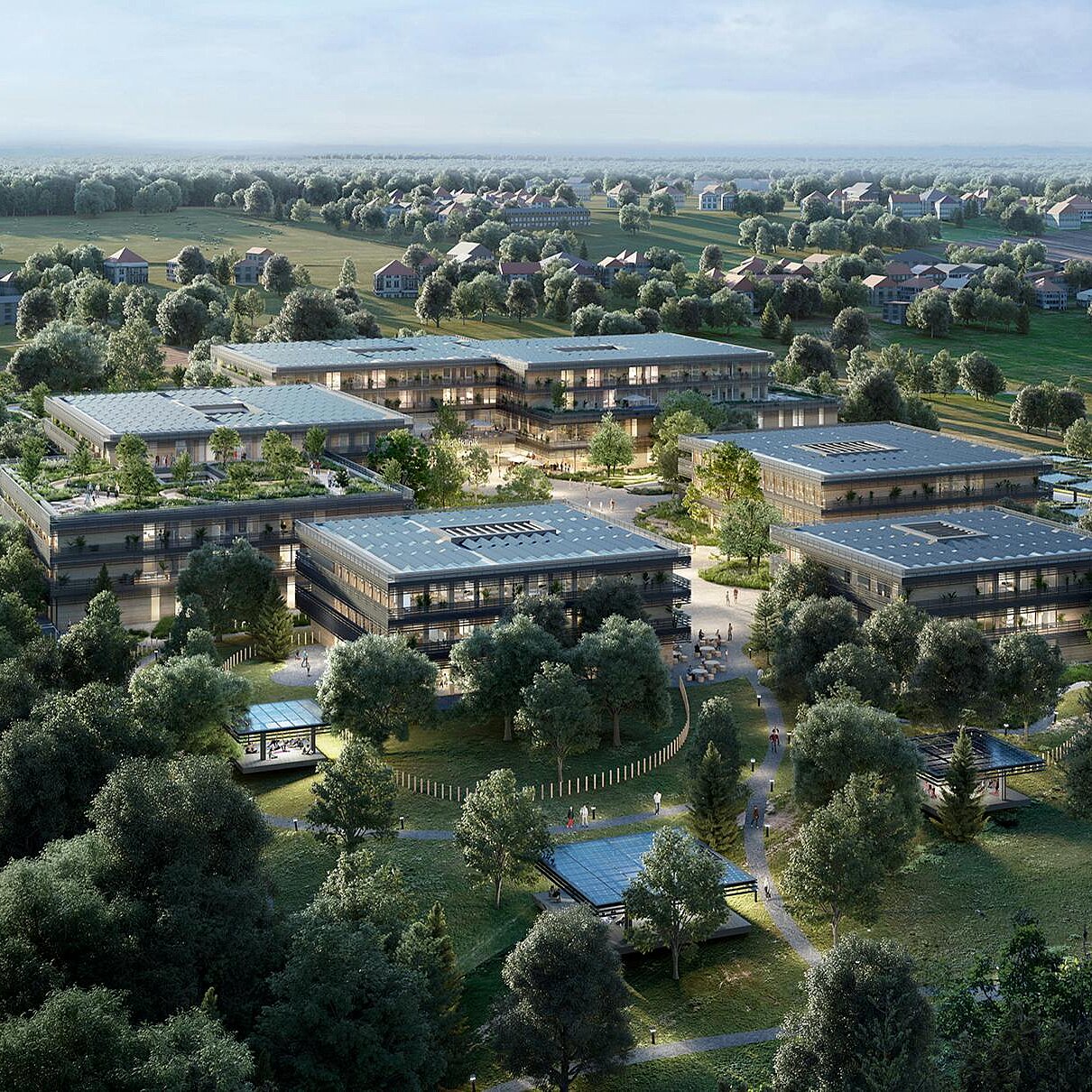 Eine luftige Ansicht eines modernen Gebäudekomplexes, umgeben von grünen Bäumen und landschaftlicher Natur. Die Architektur umfasst mehrere flache Gebäude mit großen Fenstern und begrünten Dächern, die in einer harmonischen Umgebung angeordnet sind. In der Nähe sind entspannende Grünflächen und Wege sichtbar.