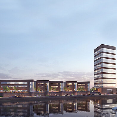 Moderne Architektur an einem Gewässer, bestehend aus einem hohen Turm und mehreren niedrigen Gebäudne. Die Fassade ist überwiegend aus Glas und dunklem Material. Umgeben von Wasser, reflektiert das Gebäude die Umgebung, während Pflanzen und Sitzbereiche das Gesamtbild ergänzen.