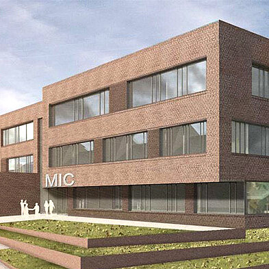 Moderne, dreigeschossige Gebäude mit einer Backsteinfassade, das mit großen Fenstern ausgestattet ist. Der Schriftzug "MIC" ist gut sichtbar im Erdgeschoss. Vor dem Gebäude befinden sich terrassenförmige Grünflächen und einige Personen, die miteinander interagieren.