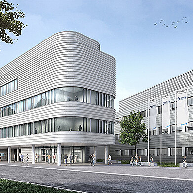 Moderne Architektur eines Gebäudes mit geschwungener Fassade und großen Fenstern. Das Gebäude hat mehrere Etagen und ist von einer grünen Umgebung sowie Menschen umgeben. Im Hintergrund sind weitere Gebäude sichtbar. Der Himmel ist überwiegend klar.