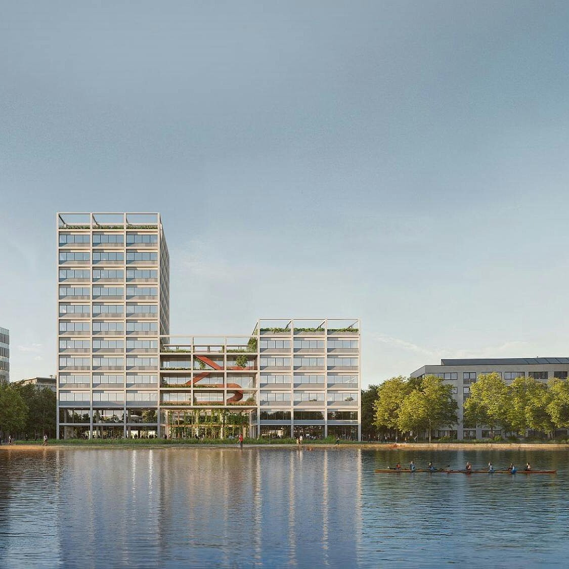 Blick auf moderne Gebäude am Ufer eines Gewässers, umgeben von Bäumen. Die Architektur ist vielfältig und zeitgenössisch, mit einer Mischung aus niedrigen und höheren Bauwerken. Der Himmel ist klar und reflektiert sich auf der Wasseroberfläche.