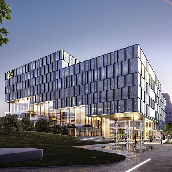 Moderne Bürogebäude mit glasierter Fassade und mehreren Etagen, umgeben von Grünflächen. Vor dem Gebäude sind Wasserspiele zu sehen. Die Architektur ist elegant und zeitgemäß, mit Sicht auf die Stadt im Hintergrund. Der Himmel zeigt einen sanften Übergang zum Abendlicht.